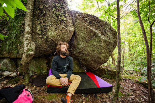 A rock climber sits at the base of a boulder, enjoying a moment