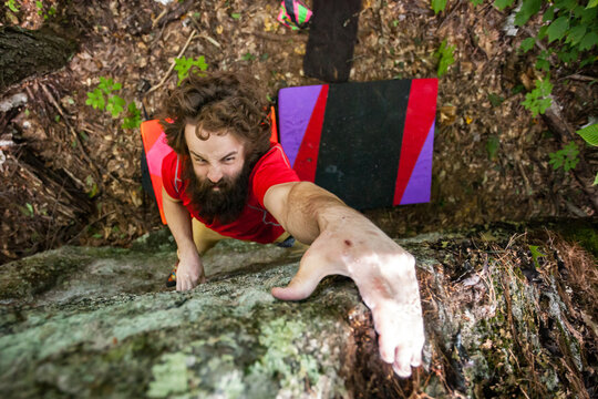 Looking down at a boulderer grimacing at the top of a climbing route