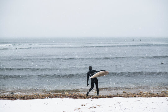 Solo Woman with surfboard on a snowy beach