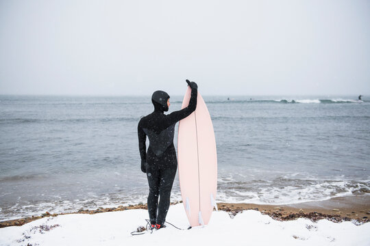 Solo Woman with surfboard going to surf in the snow