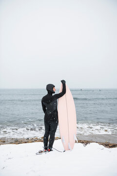 Solo Woman with surfboard going to surf in the snow