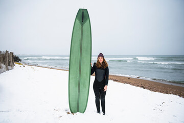 Solo woman with surfboard on snowy beach in winter