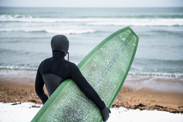 Solo Woman with surfboard on a snowy beach