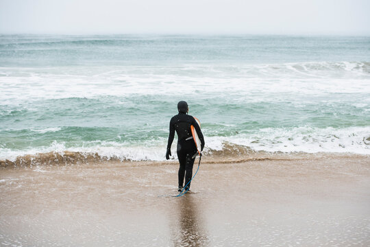 Solo woman on a winter beach going surfing while snowing