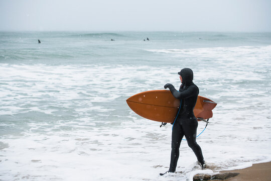 Woman on a winter beach going surfing while snowing