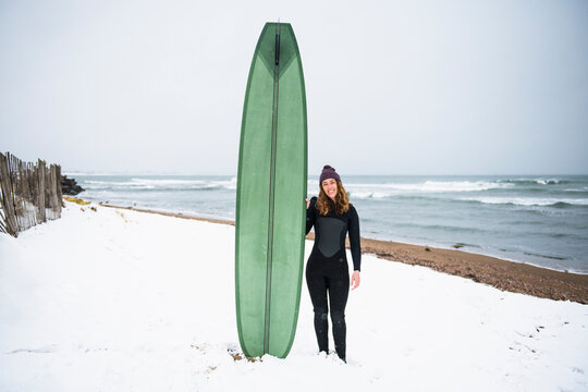 Solo woman with surfboard on snowy beach in winter