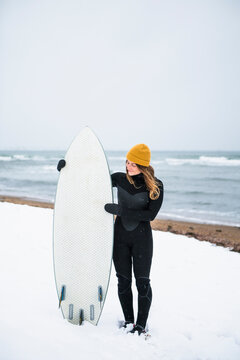 Solo woman with surfboard on snowy beach in winter