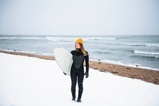 Solo woman with surfboard on snowy beach in winter