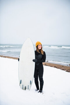 Solo woman with surfboard on snowy beach in winter