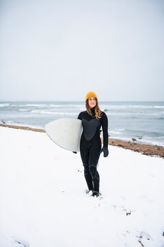 Solo woman with surfboard on snowy beach in winter