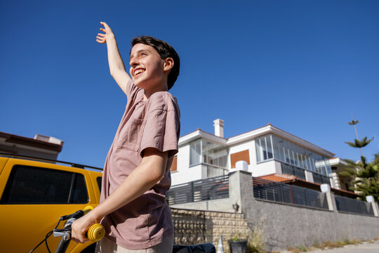 Teenager waving hand with bicycle standing on the street against taxi