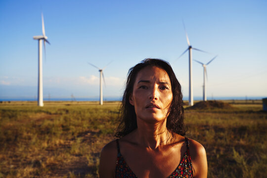 Serene contemplative woman in the field with wind turbines