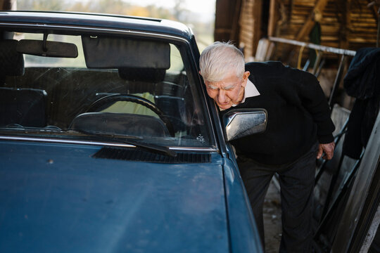 Elderly man inspecting a vintage car in a rustic barn