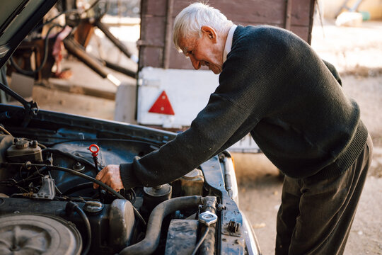 Elderly man repairs car engine in rustic garage