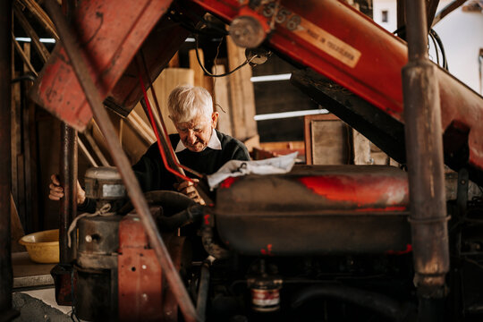 Elderly man repairing a vintage tractor in a rustic workshop