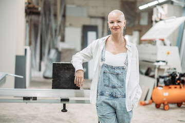 Bald woman in overalls smiling in carpentry workshop