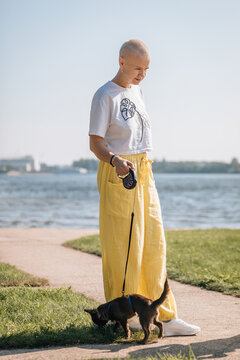 Bald woman walking chihuahua on retractable leash by riverside park