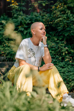 Confident bald woman in white tee and yellow pants in leafy park