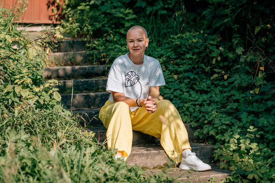 Bald woman sitting on garden steps in sunlit greenery