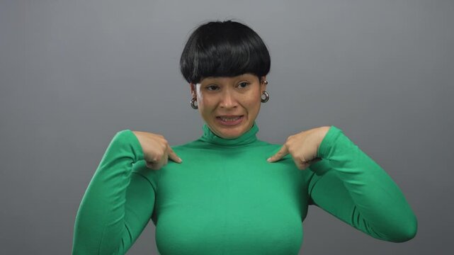 Woman in green sweater gesturing against isolated grey background expresses emotions with hands and face signifying communication and expression in a minimalist studio setting