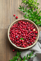 Fresh cranberries in a dark bowl on a wooden background with green branch and napkin.