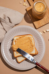 Peanut butter toast on a plate on a beige background with a knife
