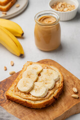 Peanut butter toast and banana on a wooden board on a light background