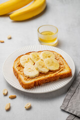 Peanut butter toast and banana in a white plate on a light background