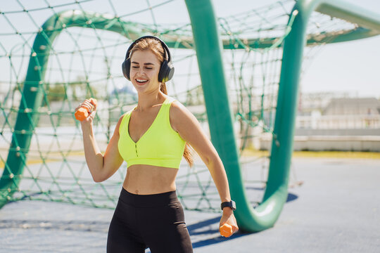 Dancing to the rhythm, a woman enjoys her workout with headphones on, feeling energized and cheerful amidst a vibrant playground setting.