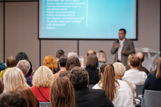 Audience listens to presenter during a business conference in modern meeting room with large screen