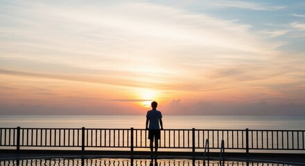 Fototapeta premium A young man stands by the pool and watches the sunset over the ocean