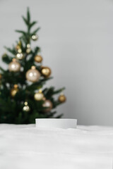 Christmas holiday background and a round miniature podium. White snow in the foreground with copy space and a blurred minimalist Christmas tree and golden ornaments.
