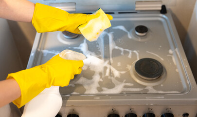 Overhead view of a hand in a yellow glove vigorously scrubbing a cooktop with suds, realistic domestic cleaning action. 