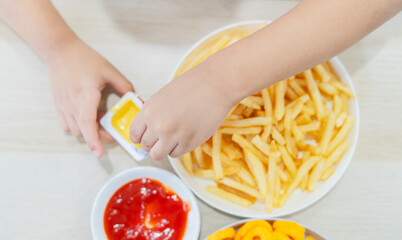 Little kid hands taking French fries from white plate with cheese dip, boy eating French fries
