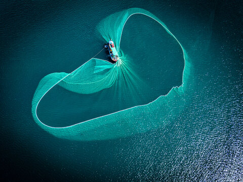 Aerial view of a vibrant green fishing net cast wide from a boat on the dark waters, creating a striking contrast, An Ninh Dong, Phu Yen, Vietnam. - Powered by Adobe