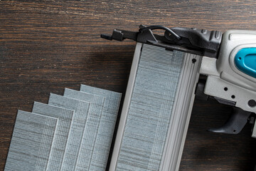 The part hammer of a power nail gun with of strips of finishing nails on wooden background. Pneumatic nail gun with metal brads, closeup, top view