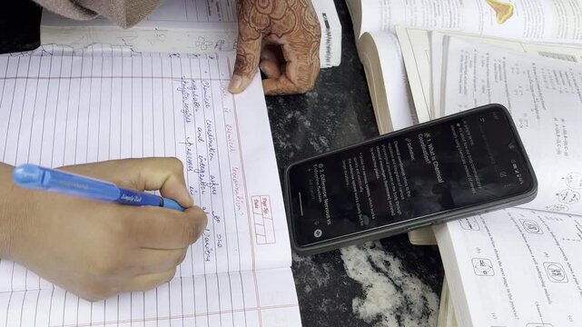 Close-up of a student's hands writing notes in a notebook, copying answers from AI chatbot displayed on a smartphone screen. A student cheating in exam using AI Chatbot to get answers of questions.