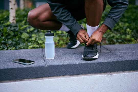 Athlete Ties Shoelaces On Park Wall With Water Bottle and Phone Nearby - Powered by Adobe
