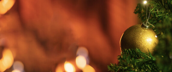 Golden Christmas bauble upon green tree branches featuring warm festive lights glowing softly within background