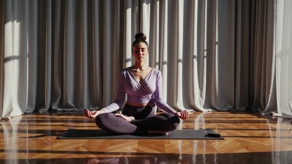 Woman practicing meditation on yoga mat. Yoga mindfulness practice in sunlit studio. Fitness wellness focus with health benefits. Exercise for mental wellbeing and meditation. Calm breathing posture.