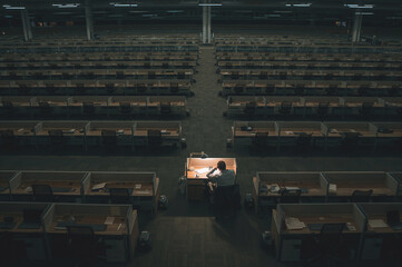 A man works alone at night in an open-plan office among many empty desks. A conceptual photo demonstrating the workload.