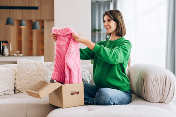 Woman unboxing online shopping clothes on sofa at home