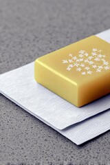 A golden bar with a white floral design sits on textured white paper, placed on a grey speckled surface.