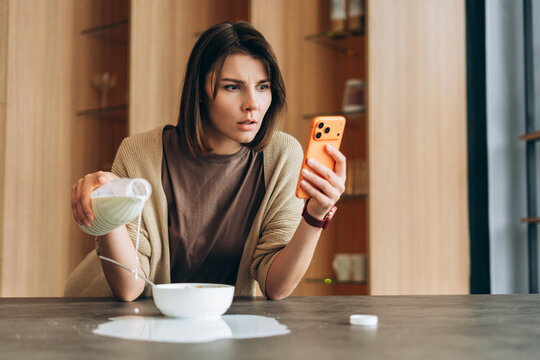 Woman distracted by phone spilling milk during breakfast