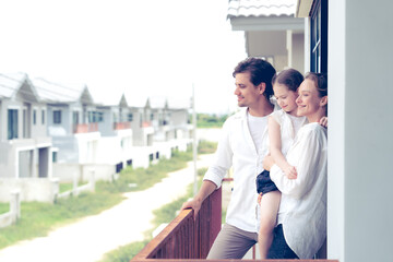 Happy family of three, parents and their young daughter, enjoying the view from the balcony of their new house. This image captures the joy and excitement of moving into a new home.