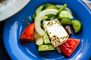 Blue plate with sliced vegetable (onion,green pepper,cucumber,tomato) and cheese with herb, olive oil.