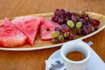3 piece of watermelon, bunch of grapes on plate and cup of coffee on table.
