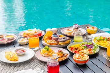 Vibrant breakfast spread on outdoor table by pool. Assorted pastries, fruits, juice in tropical setting. Perfect for culinary, travel, lifestyle themes.