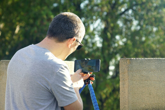 Content creator reviewing footage on tripod-mounted phone at Belgrade fortress. Symbolizes real-time editing workflow, digital nomad lifestyle, travel video production, and mobile filmmaking process.