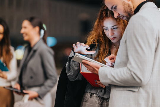 Two coworkers examine information on a tablet while notes and a red notebook are close at hand, conveying teamwork, focus, and professional collaboration in a modern office environment.